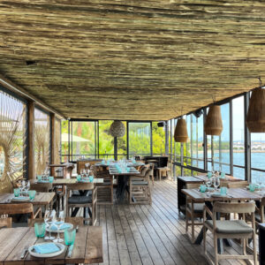 Boho-inspiriertes Strandrestaurant mit Holztischen, türkis gedeckten Plätzen und Meerblick