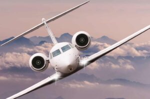 Privatjet mieten - Jet in der Luft über Wolken und Bergen, Frontansicht leicht seitlich.
