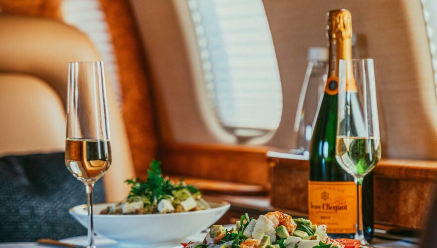 privatjet-charter-bm-concierge Stilvoll gedeckter Tisch mit Feinkost und einer Flasche Champagner im Privatjet